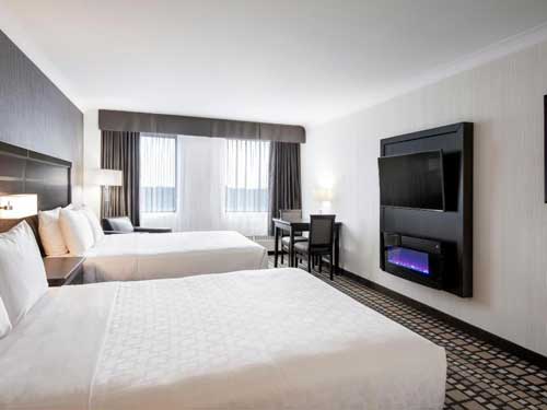 Traditional Guest Room featuring two comfortable queen size beds, dinette table with 2 chairs, and electric fireplace.